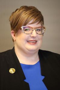 Photo of Shannon Bolger CRSP wearing glasses, a blue shirt, black blazer with a gold pin